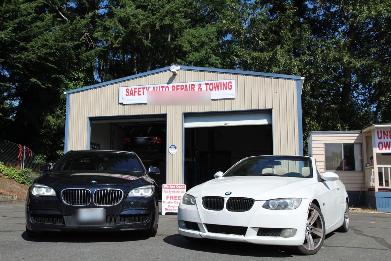 The tan corrugated-steel Bothell shop with two open bays, a black BMW 7-series and a white 3-series convertible parked out front